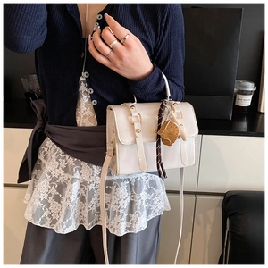 Detail of cream leather crossbody bag with studs, striped scarf and cartoon pendant