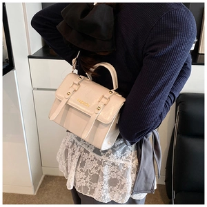 Close-up of cream-white handbag with gold FASHION lettering and buckle details
