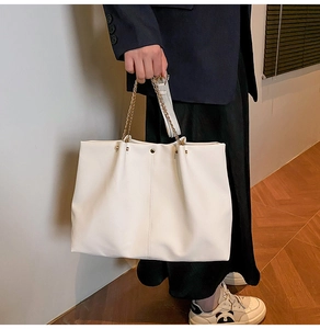 Detail of soft off-white PU leather tote bag featuring gold chain handle and draped texture