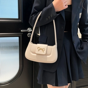 Sac baguette élégant en cuir crème avec boucle nœud doré porté sur l'épaule
