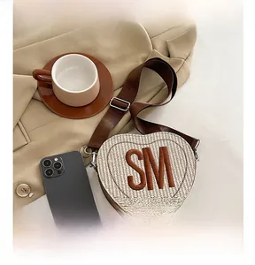 Sac bandoulière tissé en forme de cœur avec broderie SM montré à côté d'un téléphone