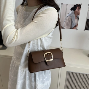 Brown leather underarm bag with gold buckle and chain strap, styled on a model