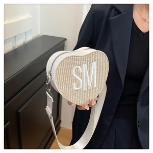 Détail du sac bandoulière blanc en forme de cœur avec texture tissée et lettres SM brodées