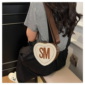 Détail d'un sac bandoulière beige tissé en forme de cœur avec broderie SM marron et large sangle