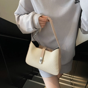 Beige woven underarm bag with metal chain and leather strap on a model