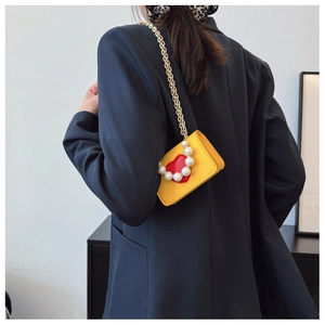 Détail du mini sac jaune avec motif cœur rouge et élégante poignée en perles blanches