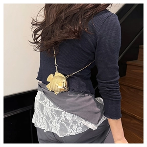 Detail of a gold fish-shaped metal crossbody bag with chain shown on a model