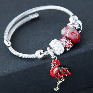 Macro detail of a silver twisted cable bracelet featuring a red flamingo and glass beads