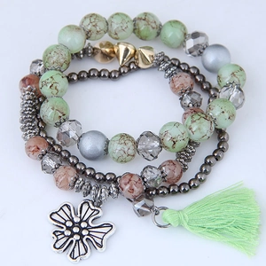 Detail of bohemian multilayer bracelet with marble beads, flower charm and green tassel