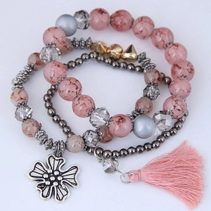 Detail of multi-layer beaded bracelet set featuring pink tassel and silver flower charm