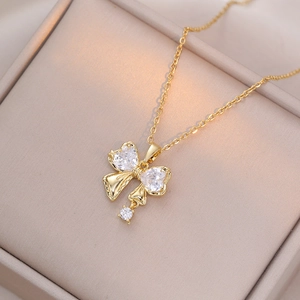 Detail of gold bow necklace with heart-shaped crystals on a beige jewelry box
