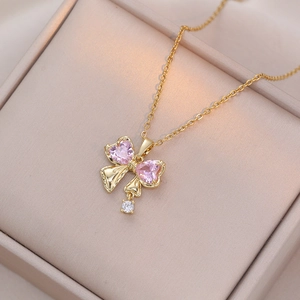 Macro detail of golden bow necklace featuring pink heart stones and a sparkling zircon