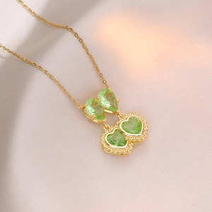 Golden double heart necklace with light green zircon stones on soft pink silk