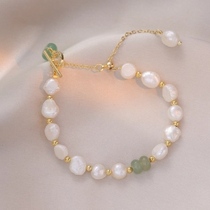 Baroque pearl bracelet with green jade bead and golden OT clasp on silk background