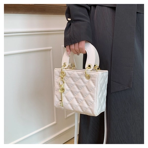 Detail of white quilted handbag with diamond pattern and gold key pendant