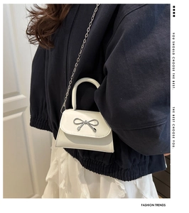 Close-up of white mini handbag featuring silver bow decoration and metal chain strap