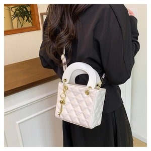 Rear view of a model carrying the white quilted leather handbag with gold metal charms