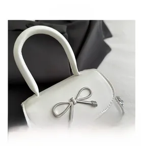 Detail of white leather handbag featuring a silver metal bow buckle and chain strap