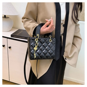 Detail of black quilted crossbody bag with golden key charm held by a model in a modern room