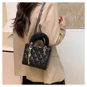 Rear view of a model wearing a black quilted square handbag with gold key pendant