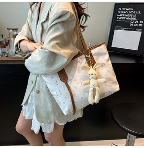 Detailed view of white printed tote bag with brown straps and cute rabbit charm accessory