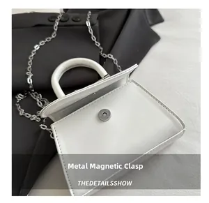 Detail of the magnetic snap closure on a mini white leather bag with silver chain