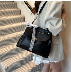 Detail of black leather tote bag featuring a white lace bow and elegant buckle closure