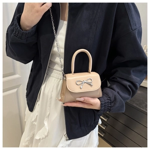 Detail of beige mini handbag featuring a silver bow buckle and elegant metal chain strap