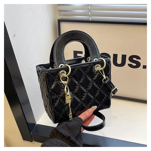 Close-up of black quilted leather handbag with gold key charm and dual top handles