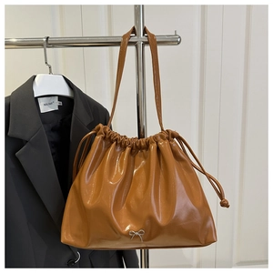 Détail du sac seau en cuir souple caramel avec cordon de serrage et décor de nœud argenté