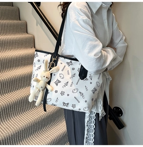 Detail view of a white tote bag with black hand-drawn prints and a plush bunny charm