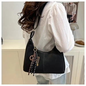 Detail of black crescent hobo bag with a decorative tassel charm and gold zipper accents
