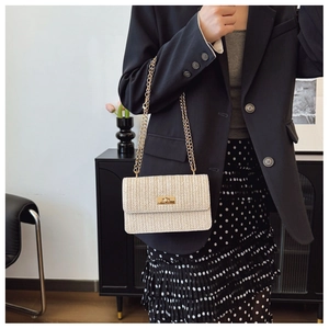 Detail view of a beige woven crossbody bag with gold metal clasp and chain strap