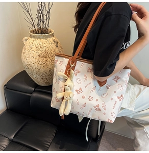 Capacity view of cream tote bag with contrast prints and plush bunny charm on shoulder