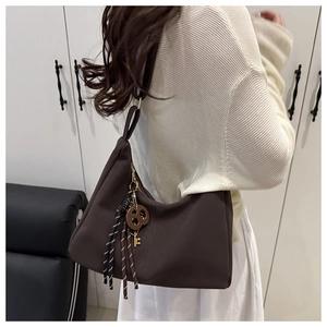 Detail of coffee brown tote bag featuring decorative fringe and metallic key pendant