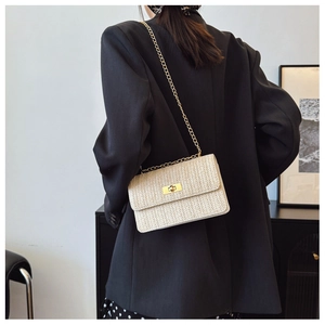 Detail view of woven straw shoulder bag featuring a gold chain and turn-lock closure