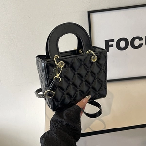Detailed close-up of black quilted lady bag with glossy finish and gold chain hardware