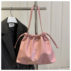 Détail d'un sac seau en cuir verni rose vif avec nœud argenté et fermeture à cordon