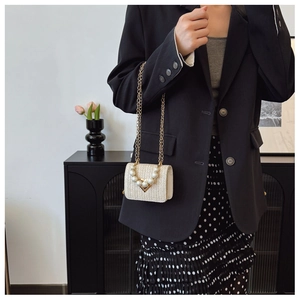 Detail of cream woven mini bag with large pearl decorations and gold chain strap on model