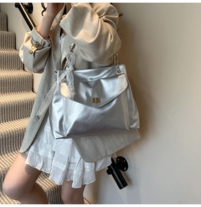 Détail du sac cabas argenté avec fermoir métallique et breloque en dentelle blanche