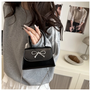 Close-up of black leather mini crossbody bag with silver metal bow and chain strap