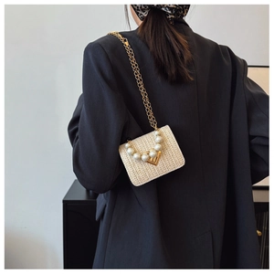 Detail of woven straw handbag with large faux pearl handle and gold chain strap