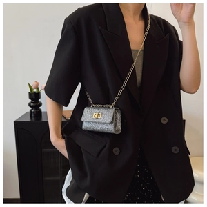 Close-up of a glittering silver mini crossbody bag with golden chain on a black blazer