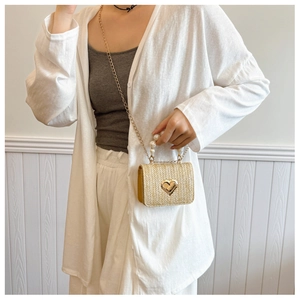 Detail of straw woven bag featuring a golden heart swivel lock and elegant pearl handle