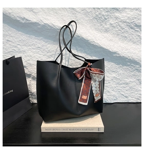 Close-up of black matte leather tote bag featuring a decorative silk scarf on stone background