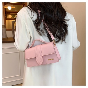 Détail du sac bandoulière rose avec rayures verticales et logo doré sur un costume blanc