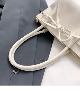 Close-up of white bucket bag with bow detail and padded handle on a grey blazer