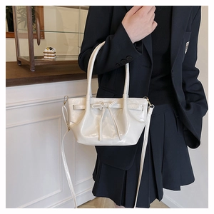 Detail of white glossy handbag with bow drawstring and adjustable metal shoulder strap