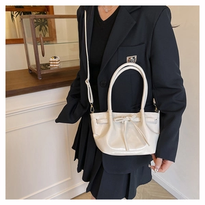 Detail of cream hand-held bucket bag with stylish bow accent and adjustable shoulder strap