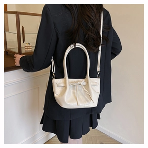 Detail of cream bow bucket bag with adjustable strap worn with a black blazer suit